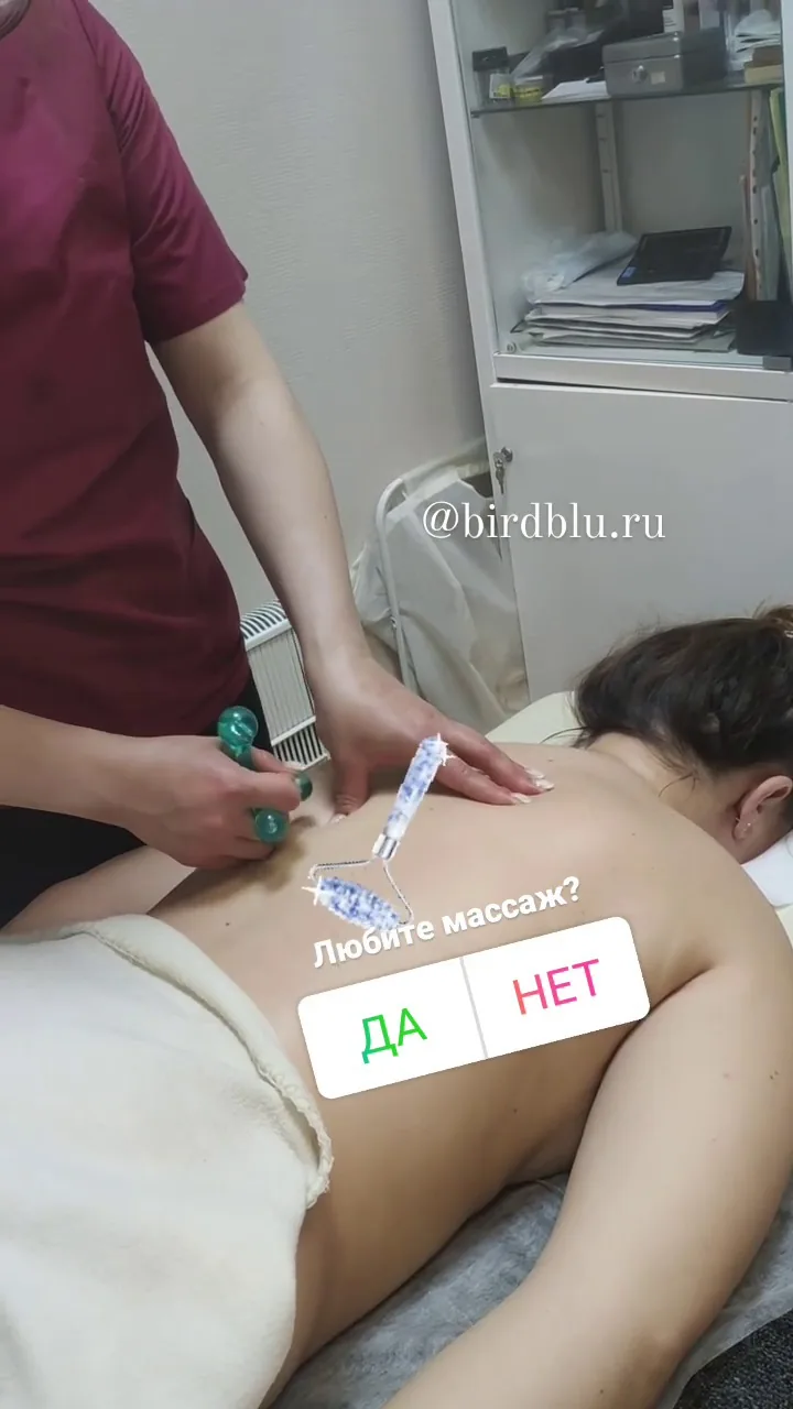 Массажист выполняет расслабляющий массаж спины и плеч с использованием специальных палочек, клиент лежит лицом вниз