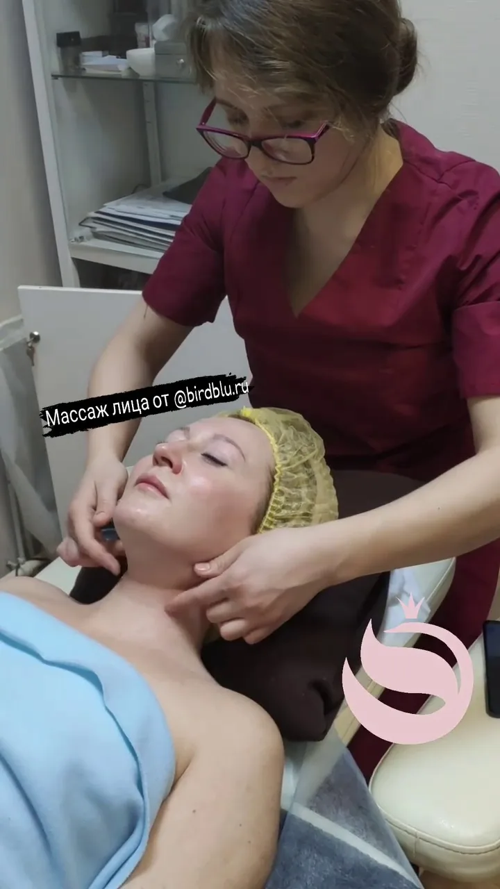 Женщина получает массаж лица в клинике, специалист в бордовом костюме проводит уходовую процедуру